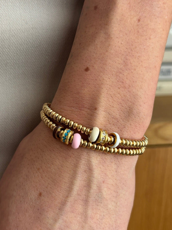 Gold bracelet with white and pink enamel beads on a wrist with a neutral background