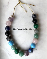 Bubblegum Necklace with multicolored beads on a white marble surface, labeled 'The Serenity Necklace'.
